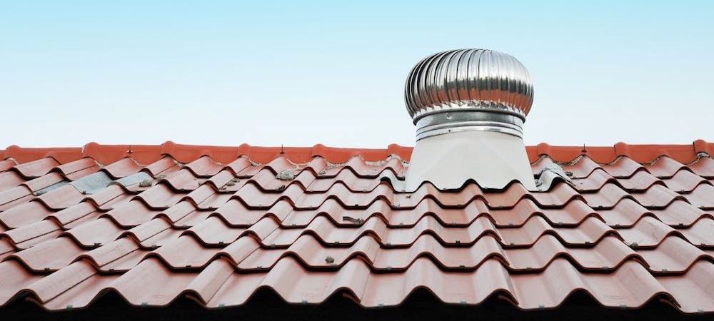 A view of an orange-tiled roof adorned with a chimney ventilator. The orange tiles create a sense of warmth and character.